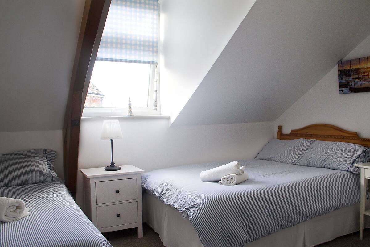 A small, clean room with two beds, a nightstand, a lamp, and a window with a view of buildings.
