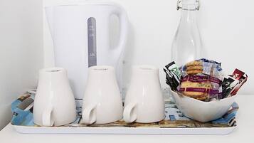 Una bandeja con tres tazas blancas, una tetera blanca y una botella de vidrio con tapón de corcho.