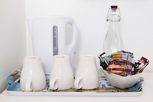 Una bandeja con tres tazas blancas, una tetera blanca y una botella de vidrio con tapón de corcho.