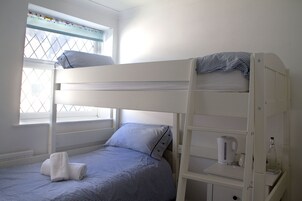 Una cama litera con ventana, una mesita de noche pequeña con una tetera y una botella.