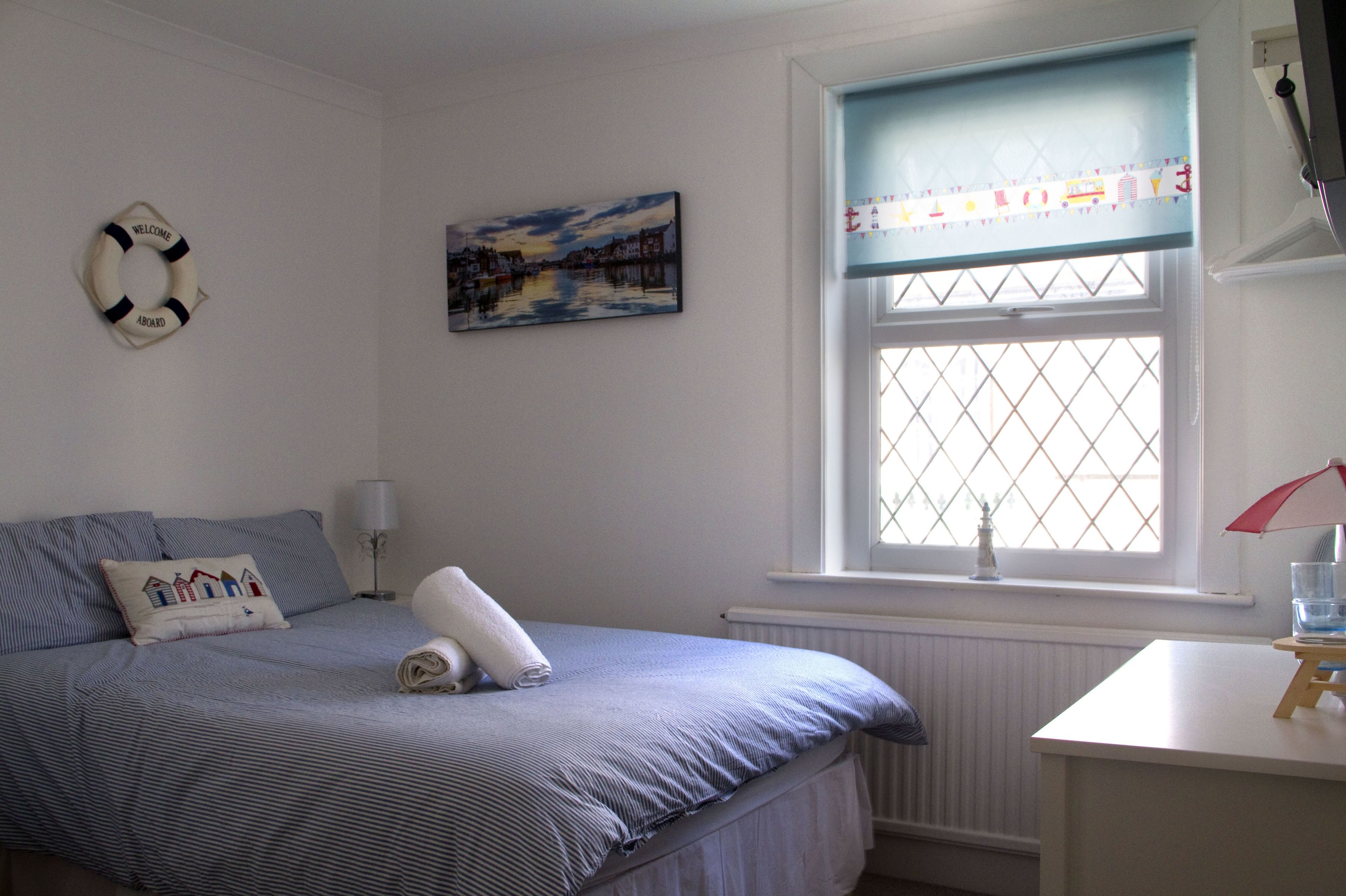 A bedroom with a bed, a window with a view, a lamp, and a life preserver on the wall.