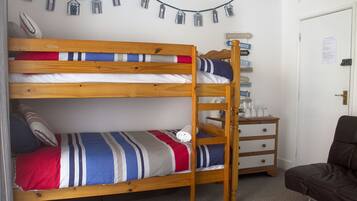 Una cama individual superpuesta con ropa de cama a rayas, un aparador de madera y una puerta con un cartel.