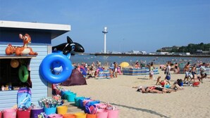 A beach with a lifeguard station, inflatable toys, and beachgoers. - Timrick Lodge Hotel (Weymouth)
