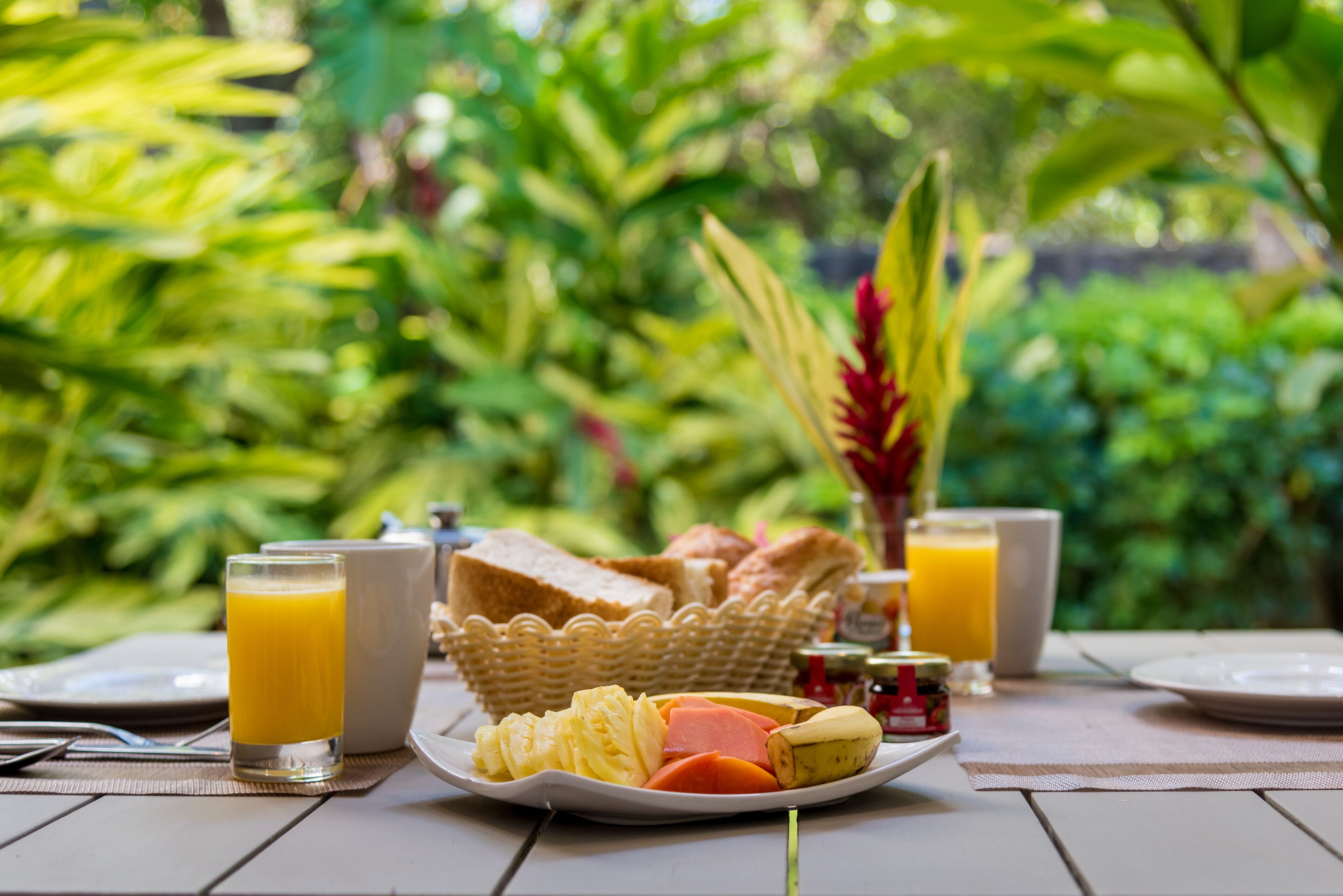 Una mesa de desayuno con un plato de comida, un vaso de zumo de naranja y una cesta de pan.