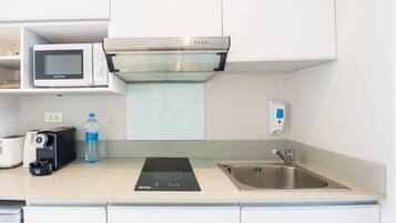 Una cocina equipada con microondas, tostadora, botella de agua, placa de inducción y pileta de acero inoxidable.
