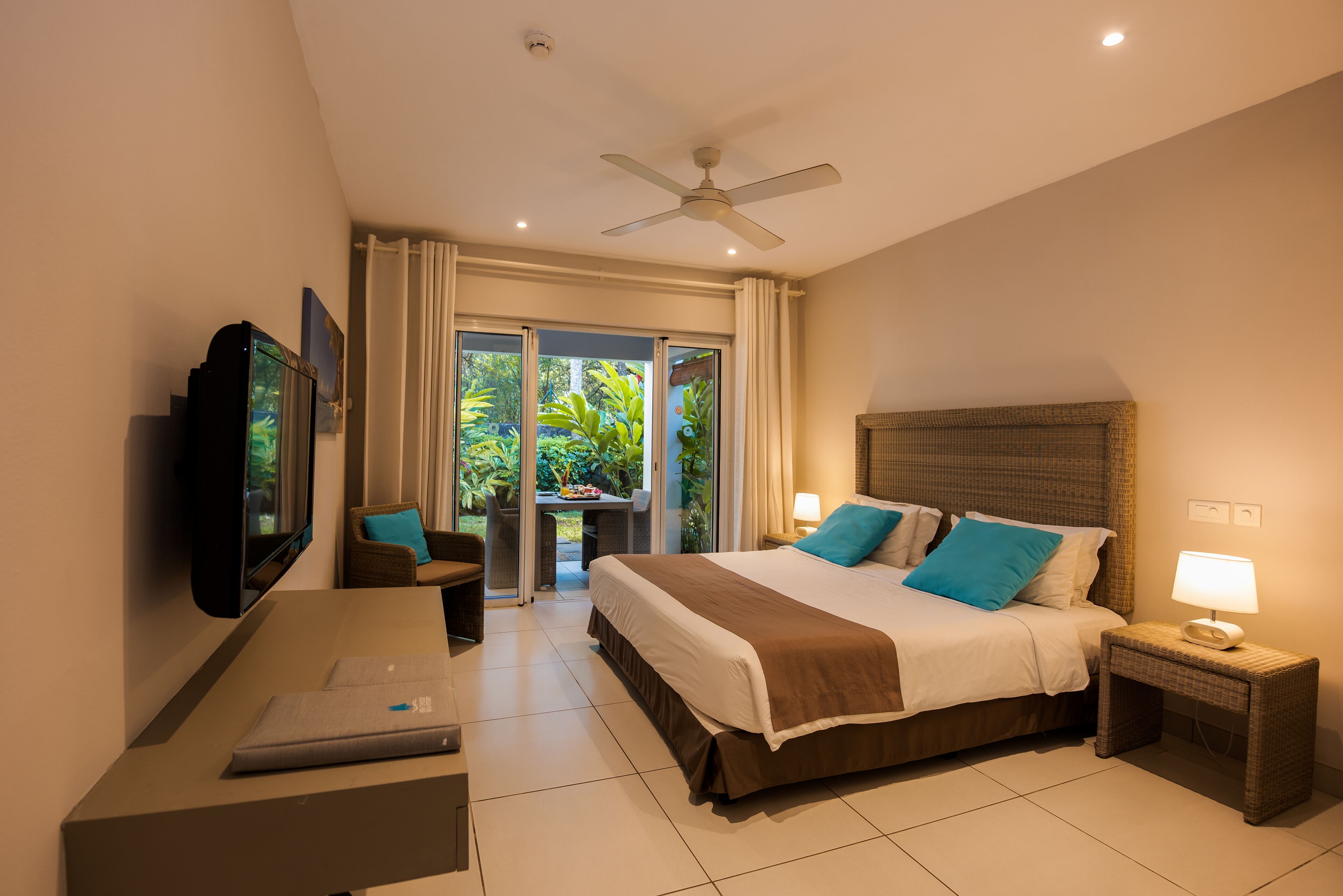 A hotel room with a bed, a desk with a laptop, a television, and a ceiling fan.