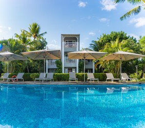 A swimming pool with lounge chairs and umbrellas, surrounded by palm trees and a building with balconies. - Mon Choisy Beach R. (Mont Choisy)