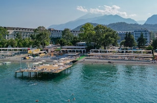 Un hotel frente al agua con muelle, playa y montañas al fondo.