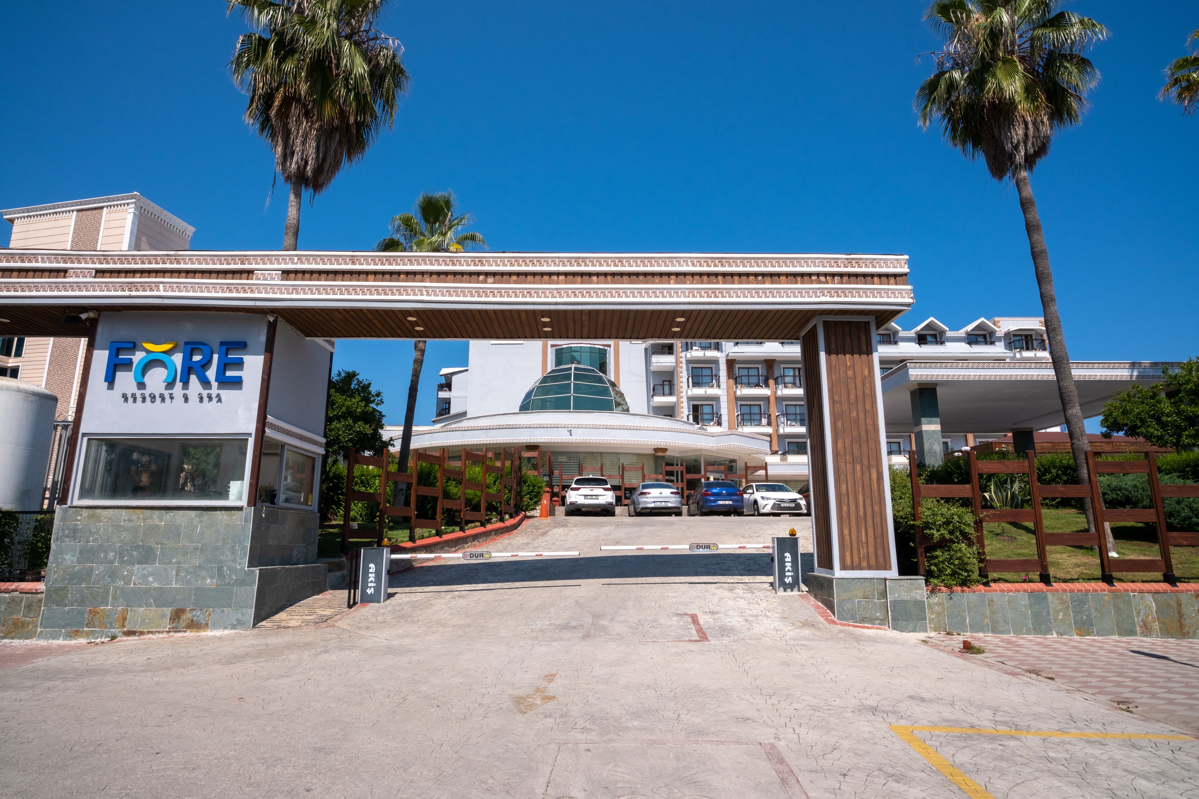 A hotel entrance with a covered driveway, palm trees, and parked cars.