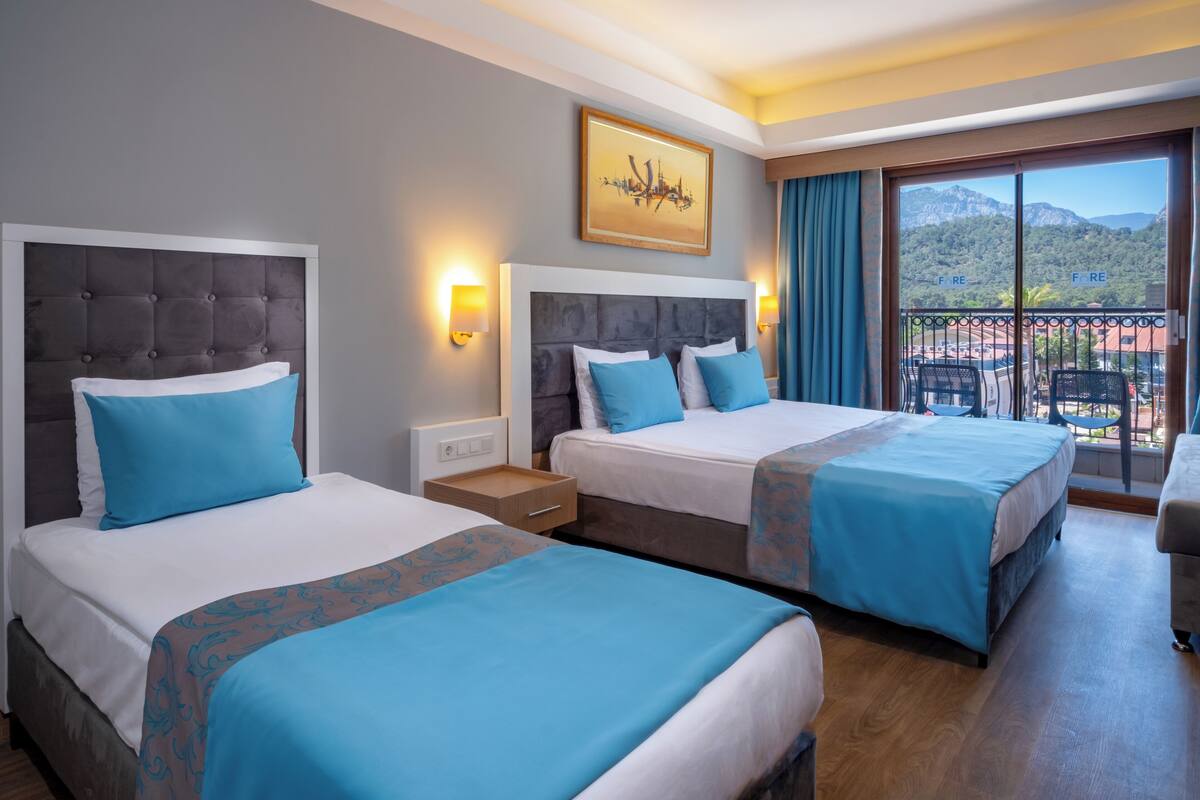 A hotel room with two beds, a balcony with a mountain view, and a painting on the wall.