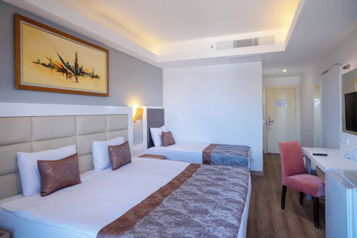 A hotel room with two beds, a desk, a chair, a TV, and a painting on the wall.