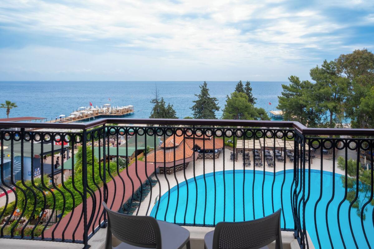 A poolside area with a view of the sea, a deck with outdoor seating, and a fenced balcony.