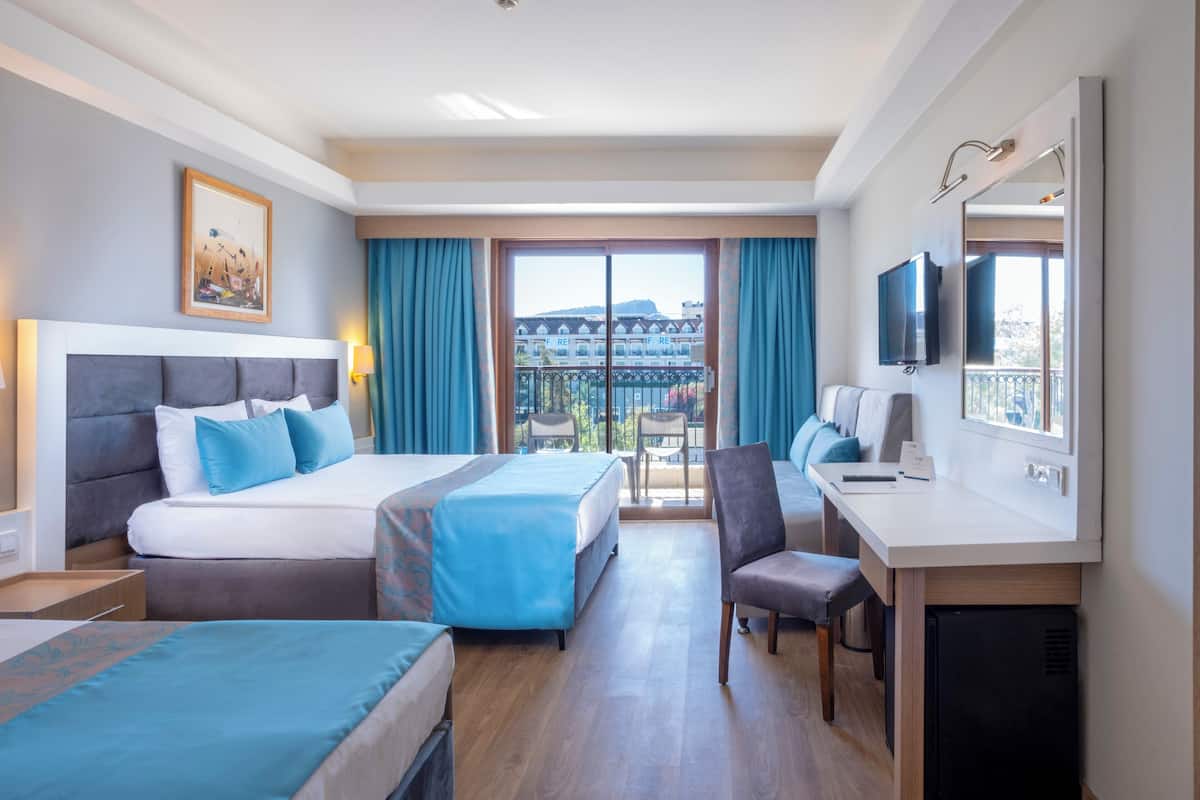 A hotel room with two beds, a desk, a chair, a television, and a large window with a view of buildings.