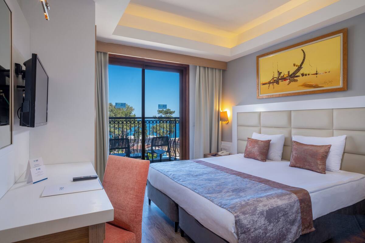 A hotel room with a bed, a desk, a chair, a TV, and a balcony with a view.
