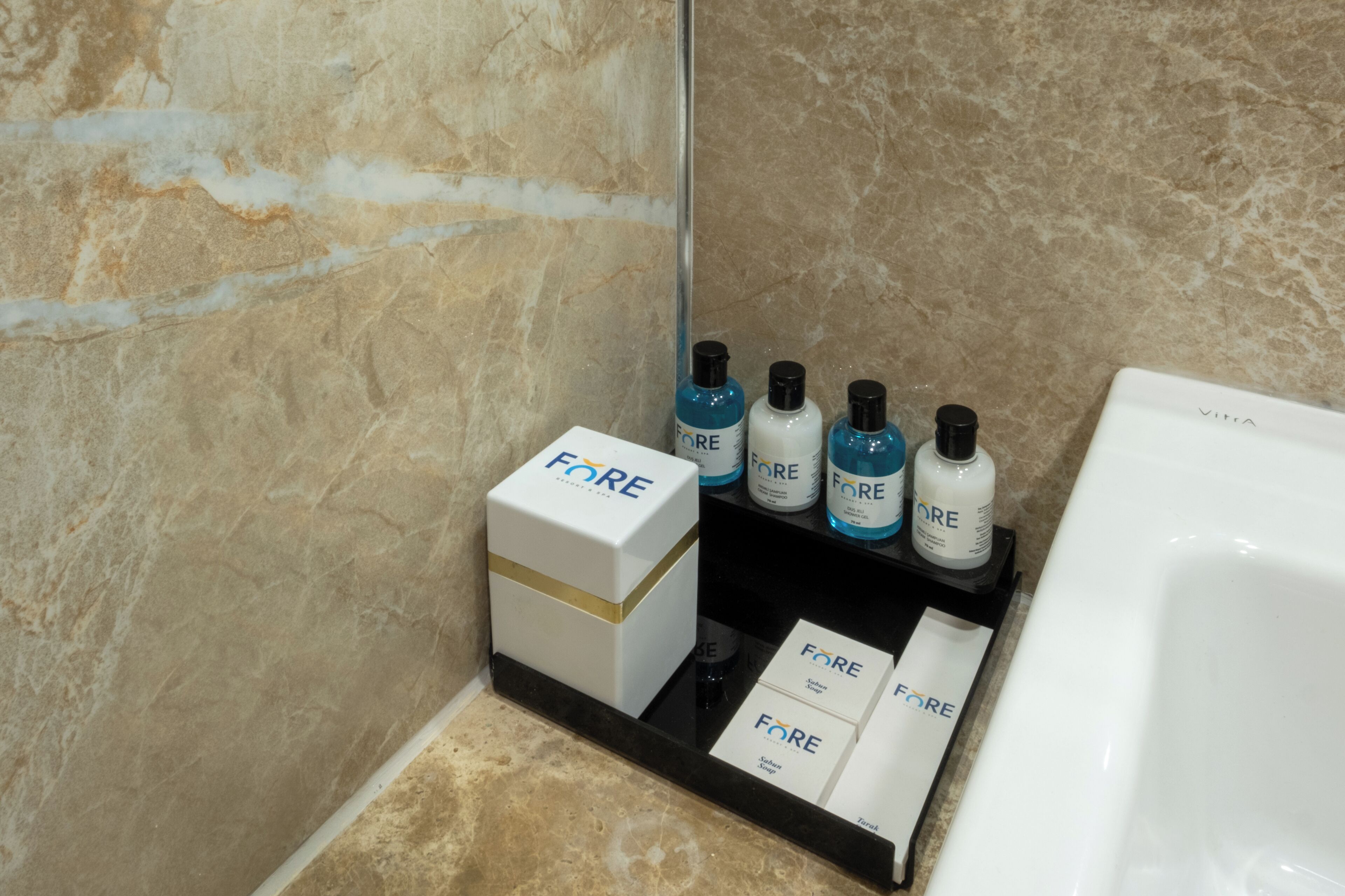 A bathroom with a marble wall, a white sink, and a shelf with FORE toiletries.
