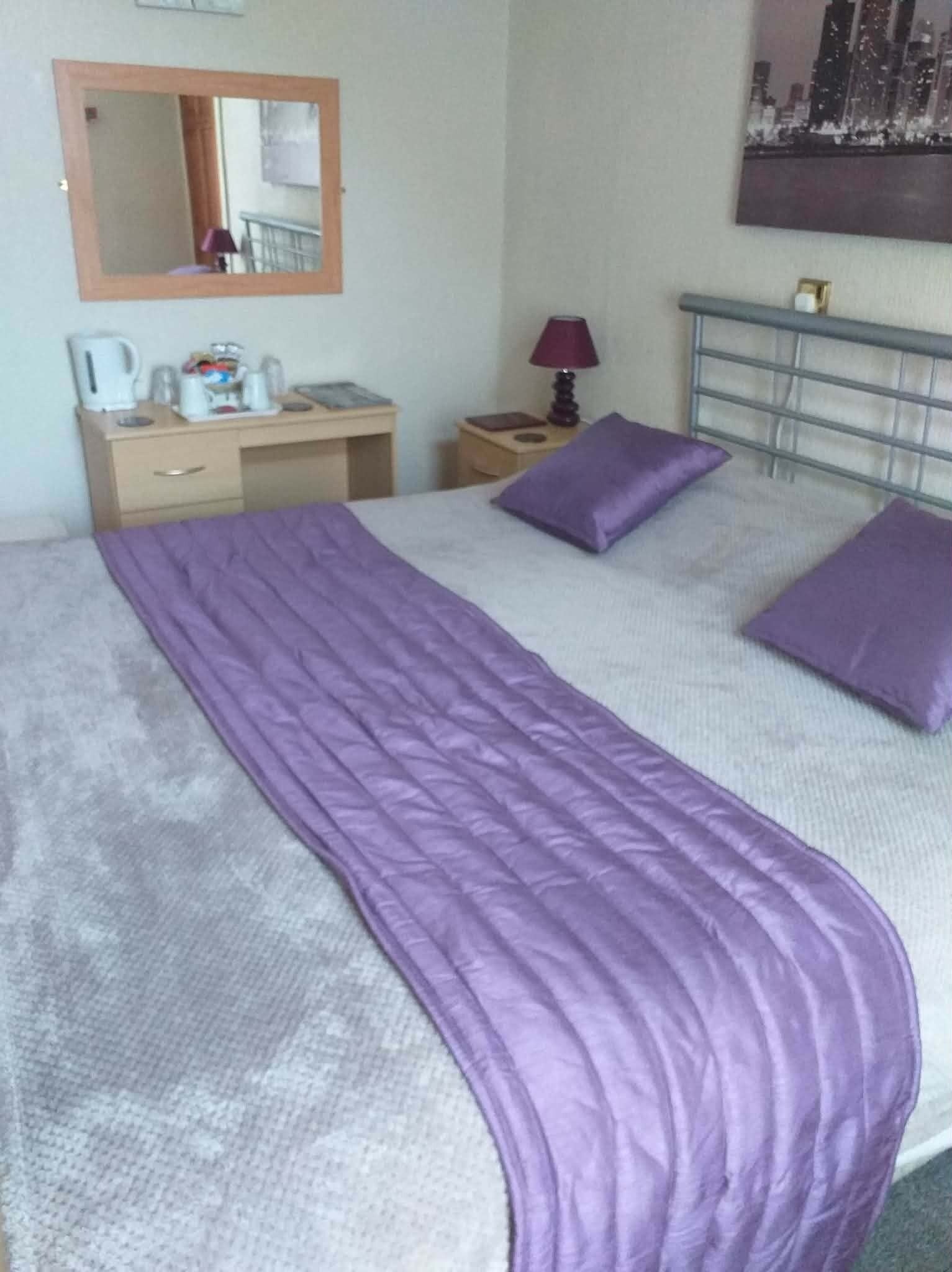 Et hotelværelse med seng, skrivebord, stol, lampe, spejl og et billede på væggen.
