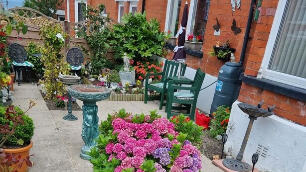A garden with a variety of plants and flowers, a wooden fence, and outdoor furniture. - Bryn Coed Guest House (Colwyn Bay)