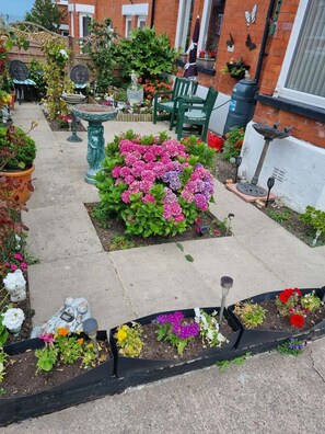A garden with a variety of plants and flowers, a wooden fence, and outdoor furniture. - Bryn Coed Guest House (Colwyn Bay)