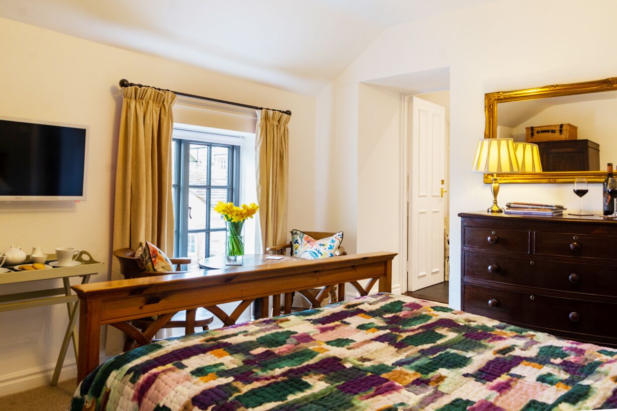 Une chambre à coucher comprenant un lit, un bureau avec une chaise, une commode, un téléviseur et une fenêtre avec des rideaux.