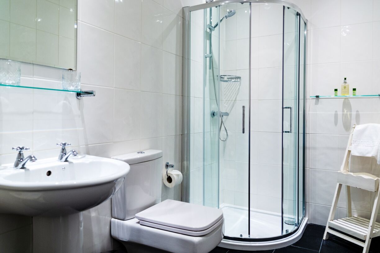 Een moderne badkamer met een glazen douchecabine, een witte wastafel en een toilet.