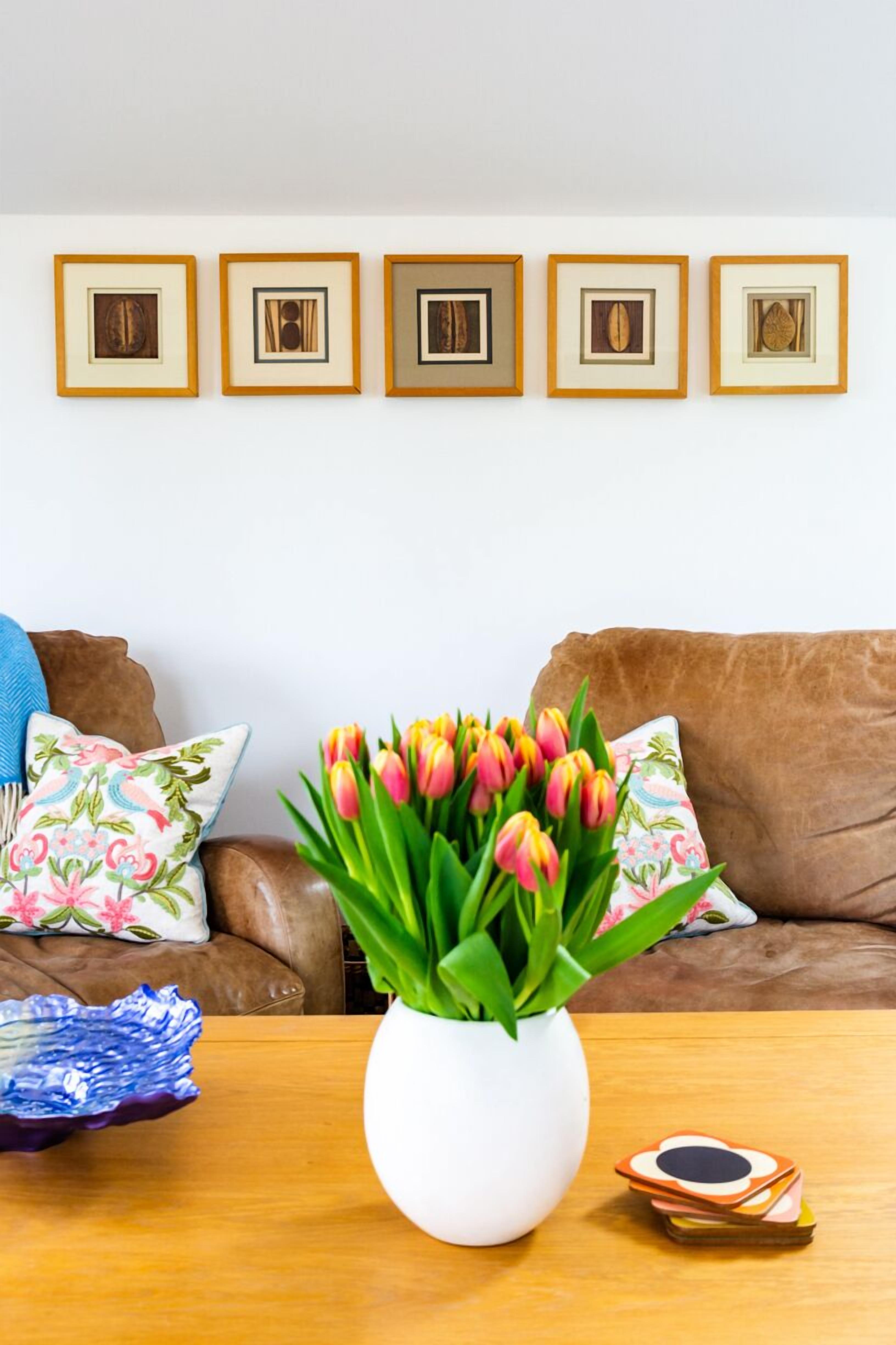 A living room with a brown leather sofa, a white vase with tulips, and framed pictures on the wall.