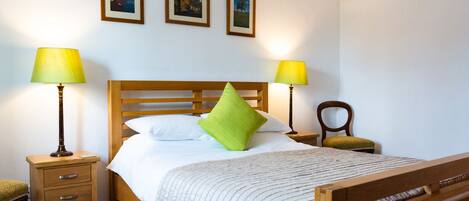 A neatly made bed with a wooden headboard, two bedside lamps, a small wooden nightstand with drawers, and a chair.