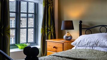 A bedroom with a bed, a nightstand with a lamp, a window with curtains, and a view of the outside.