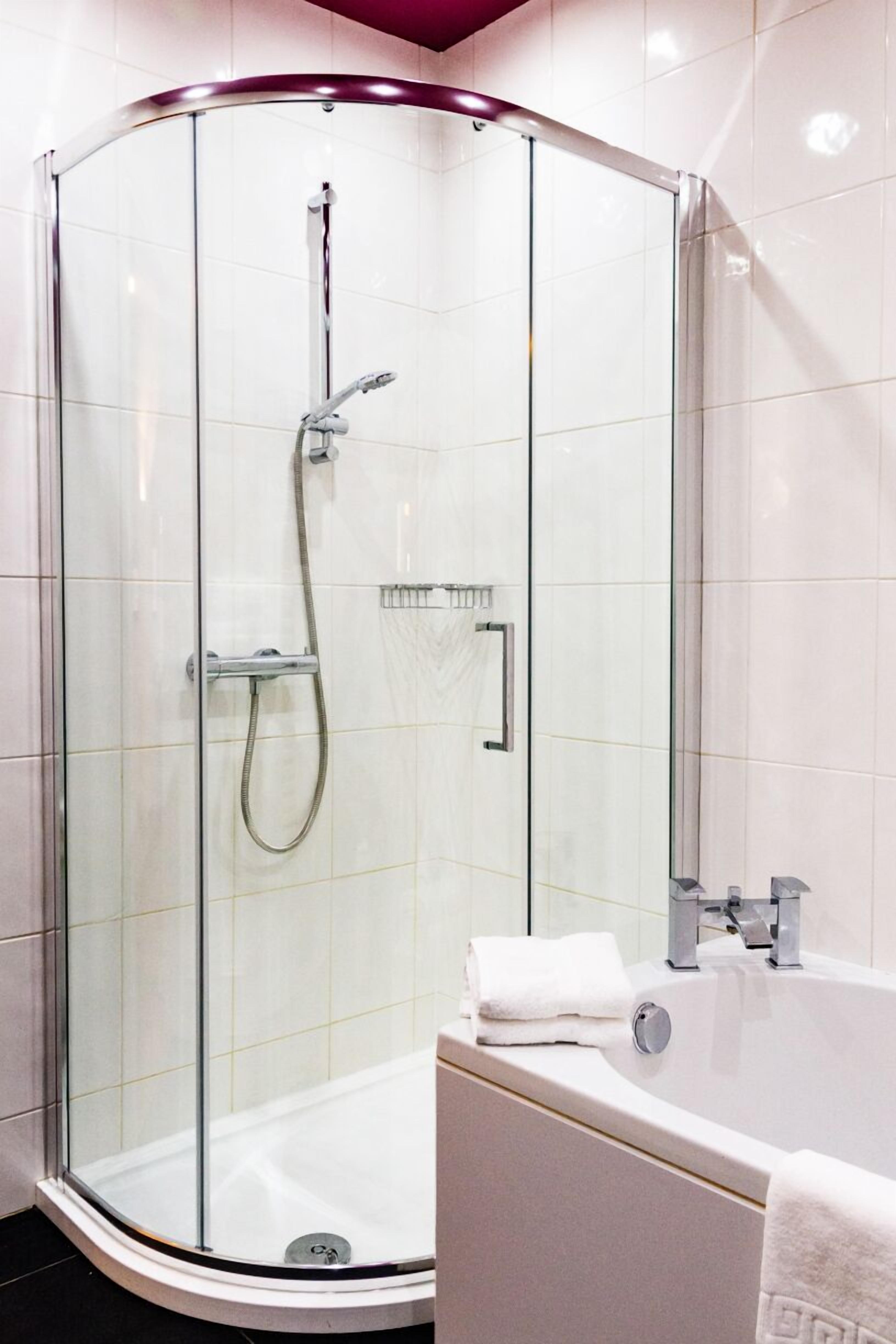 Un baño moderno con ducha envuelta en vidrio, una bañera blanca y un perchero para toallas.