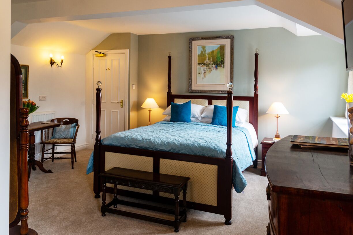 A bedroom with a four-poster bed, two bedside tables, a chair, and a bench.