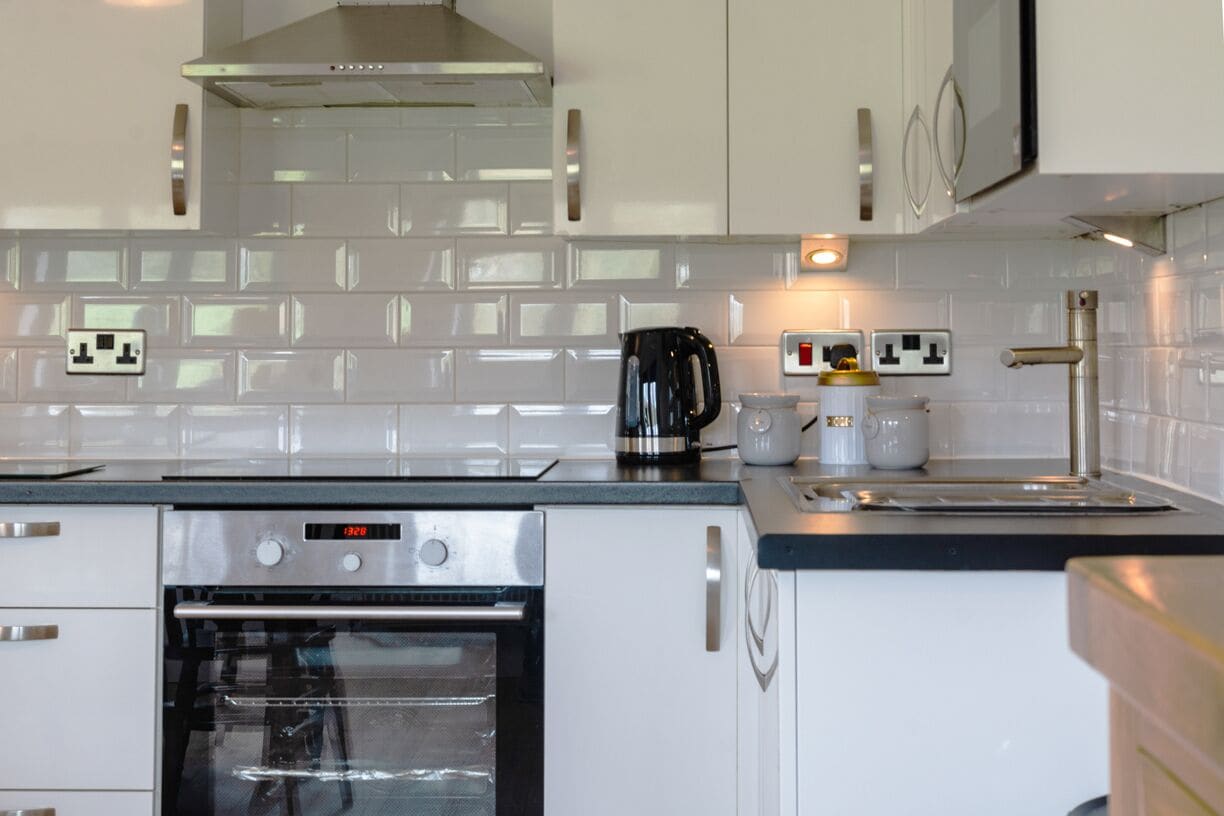 A modern kitchen with white cabinets, a stainless steel oven, a coffee maker, and a kettle.