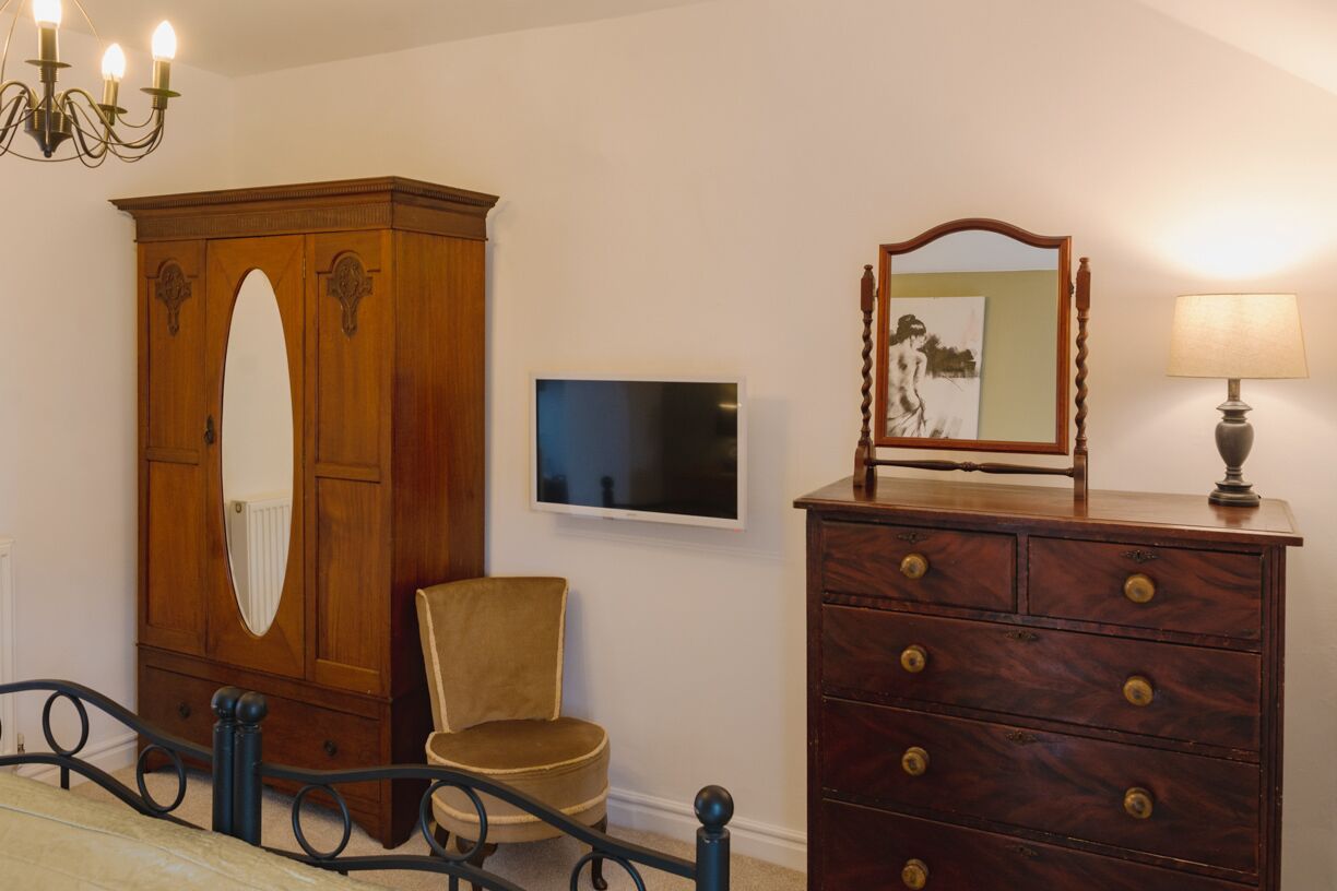 A bedroom with a wooden wardrobe, a chair, a television, and a dresser with a mirror.
