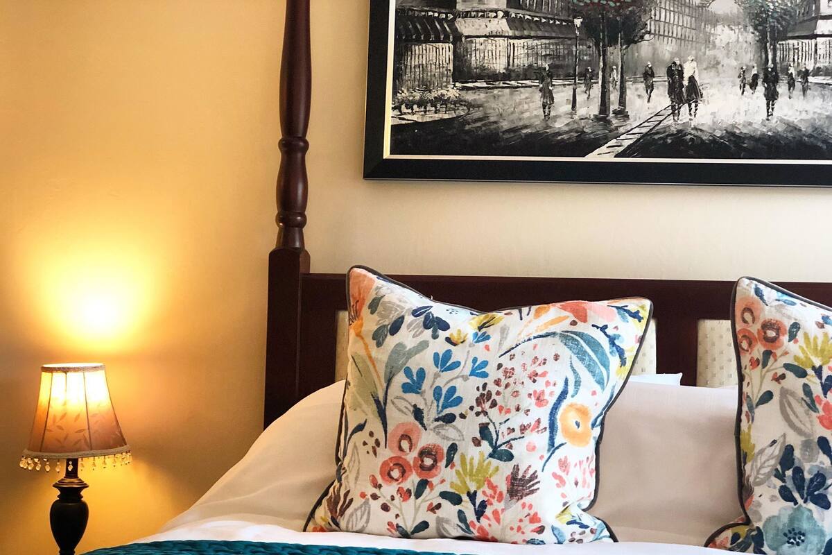A neatly made bed with floral pillows, a wooden headboard, and a lamp on the side.