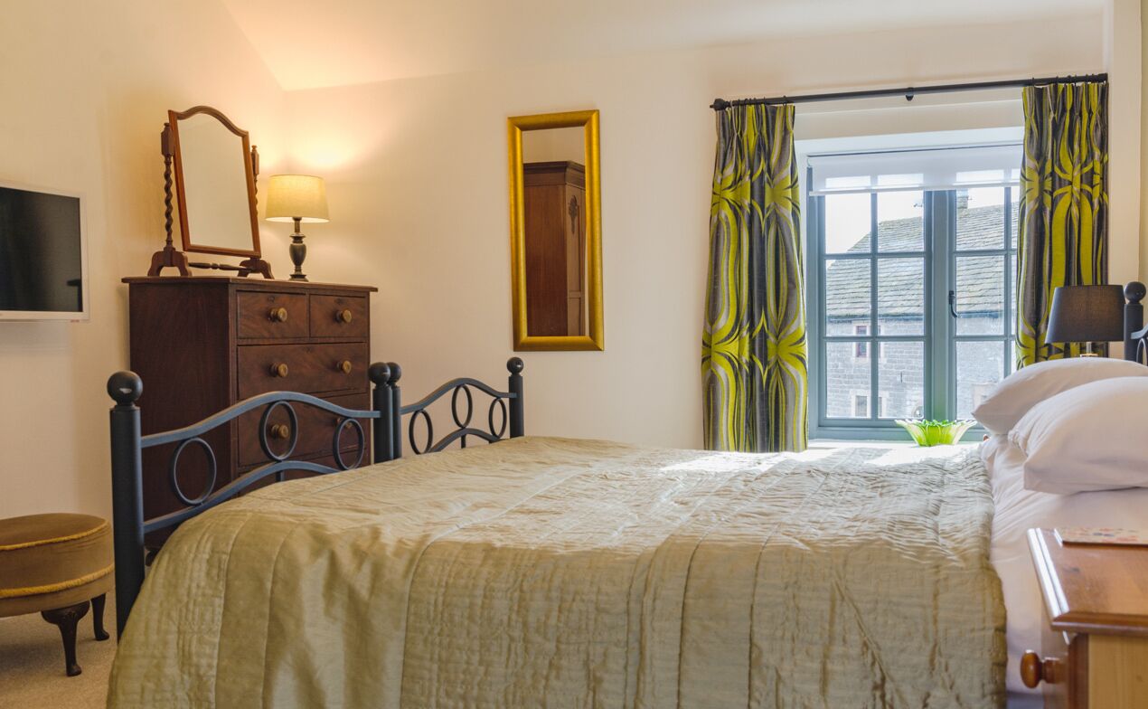 Un dormitorio con cama, cómoda, espejo y ventana con cortinas.