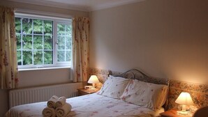 A neatly made bed with rolled towels, two bedside lamps, and a window with curtains. - Cefn Uchaf Guesthouse (Garndolbenmaen)