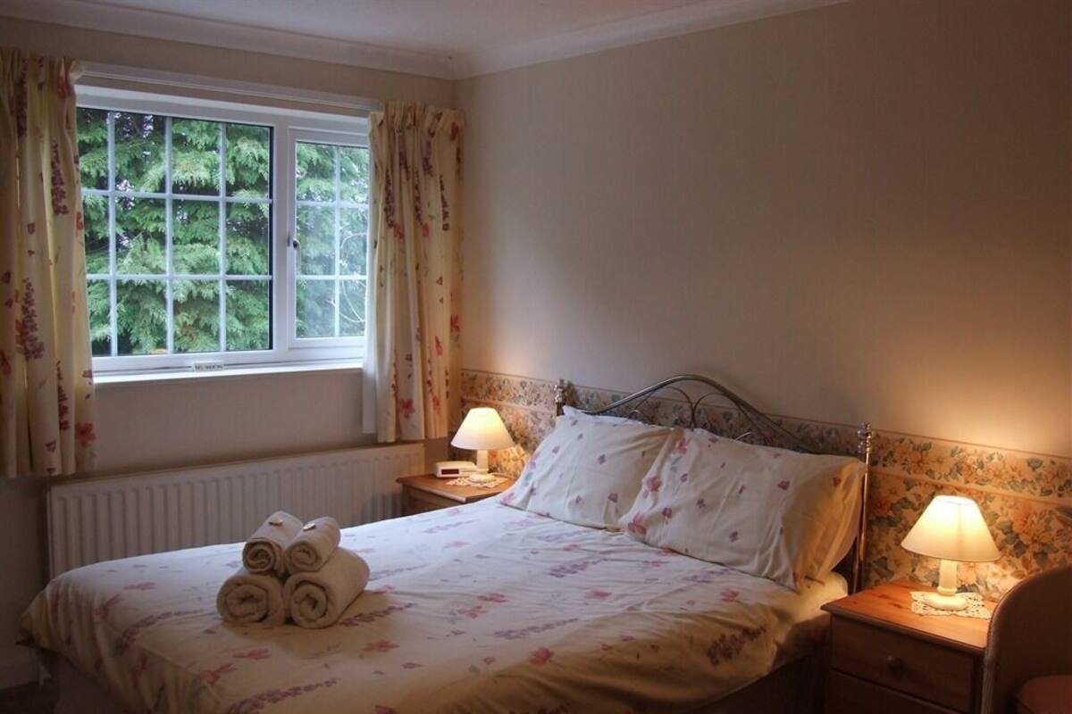 A neatly made bed with rolled towels, two bedside lamps, and a window with curtains.