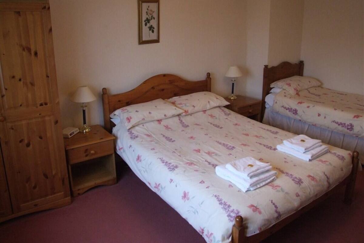 A bedroom with two single beds, wooden nightstands, a wardrobe, and a floral-patterned bedspread.