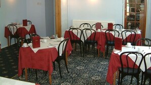A dining area with tables set for four, each with a red tablecloth and black chairs. - Cefn Uchaf Guesthouse (Garndolbenmaen)