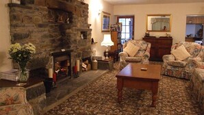 A cozy living room with a stone fireplace, floral-patterned sofas, and a patterned carpet. - Cefn Uchaf Guesthouse (Garndolbenmaen)