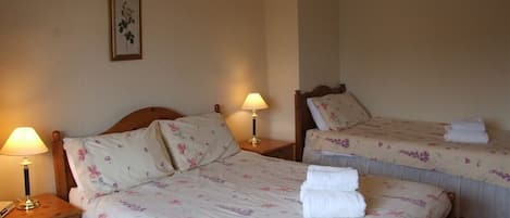 A hotel room with two beds, each with floral bedding and a nightstand with a lamp.