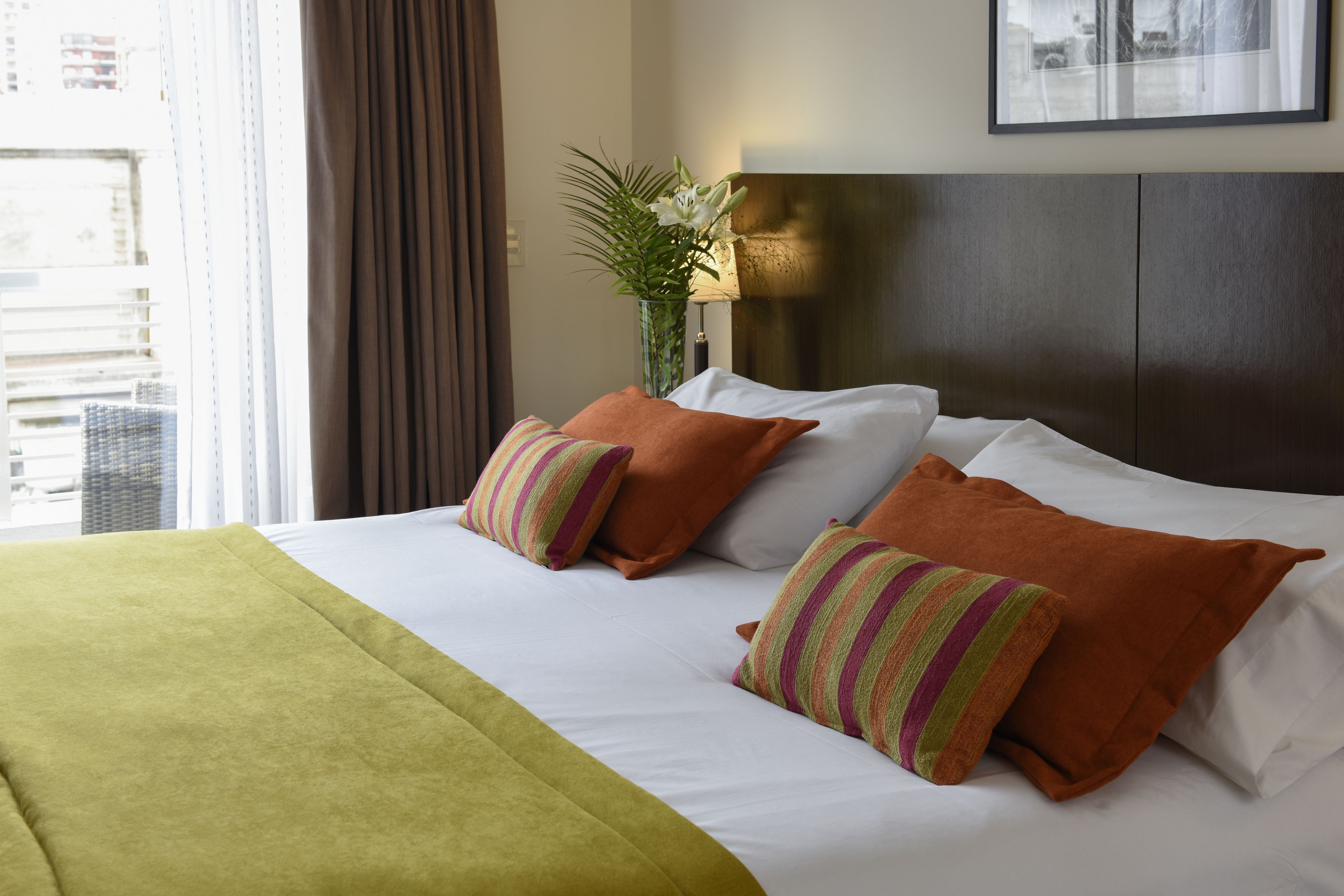 A hotel room with a large bed, a green throw blanket, and two pillows with striped patterns.
