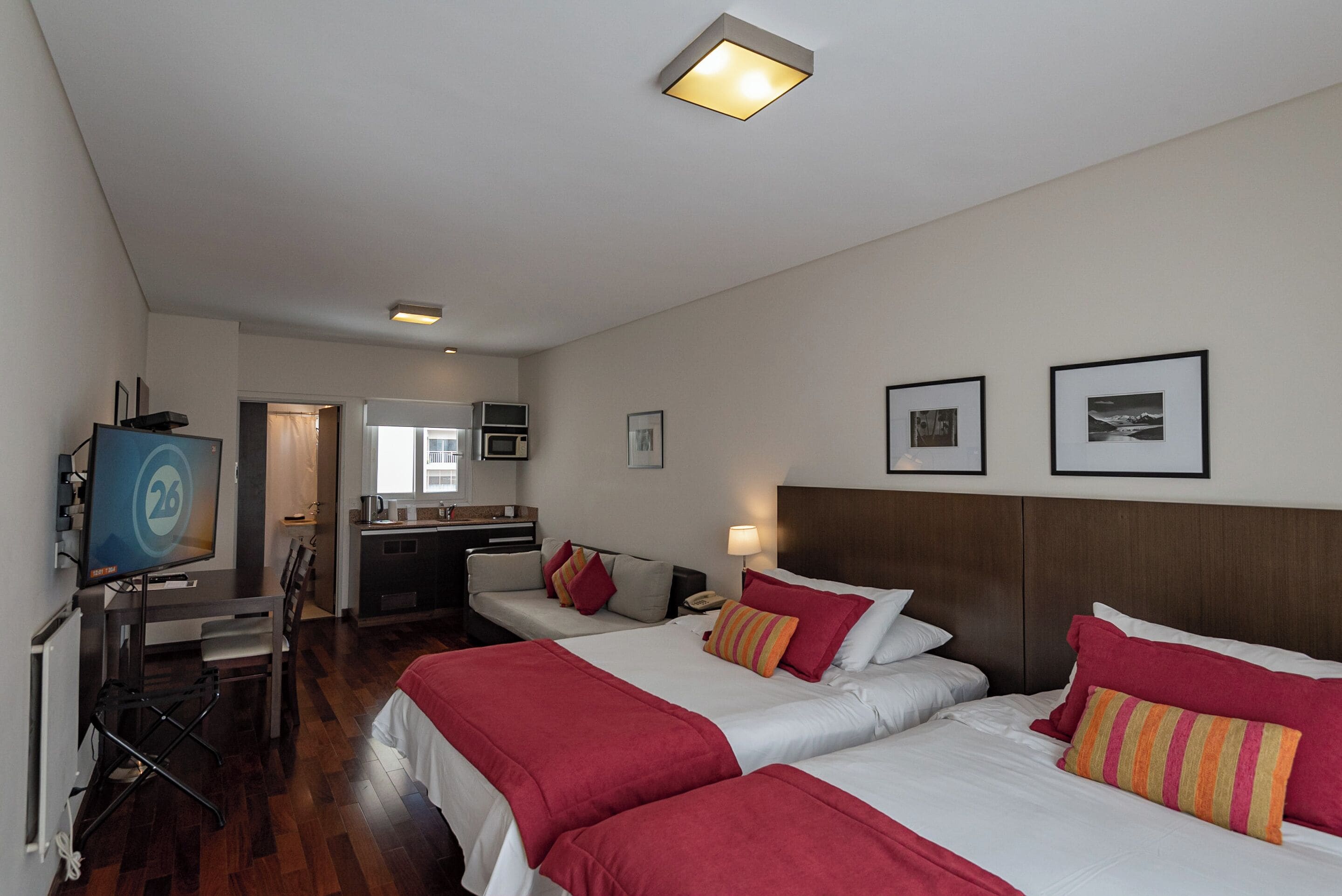 Een hotelkamer met twee bedden, een bureau, een televisie, een kitchenette en een badkamer.