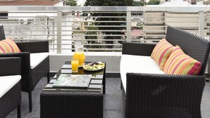 Una terraza en la azotea con mobiliario de mimbre, una mesa con una revista y una bandeja de frutas, y vistas a la ciudad.