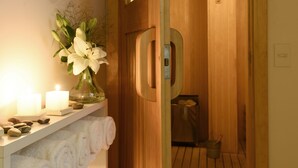 Puerta de madera que da a un sauna, con un perchero y una vela encendida sobre una repisa.