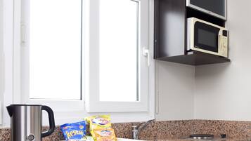 Et køkken med elkedel, mikrobølgeovn og en bordplade med snacks.