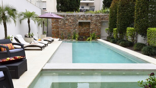 Una piscina con sillas de descanso y un muro de piedra.