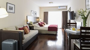 Habitación de hotel con sofá, cama, mesa de comedor con sillas, televisor y ventana con cortinas.
