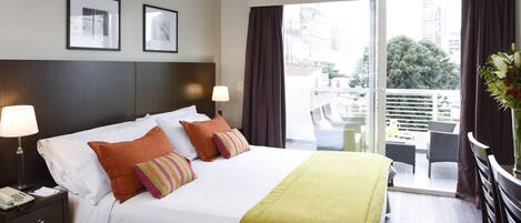 A hotel room with a bed, two bedside lamps, a window with curtains, and a view of the city.
