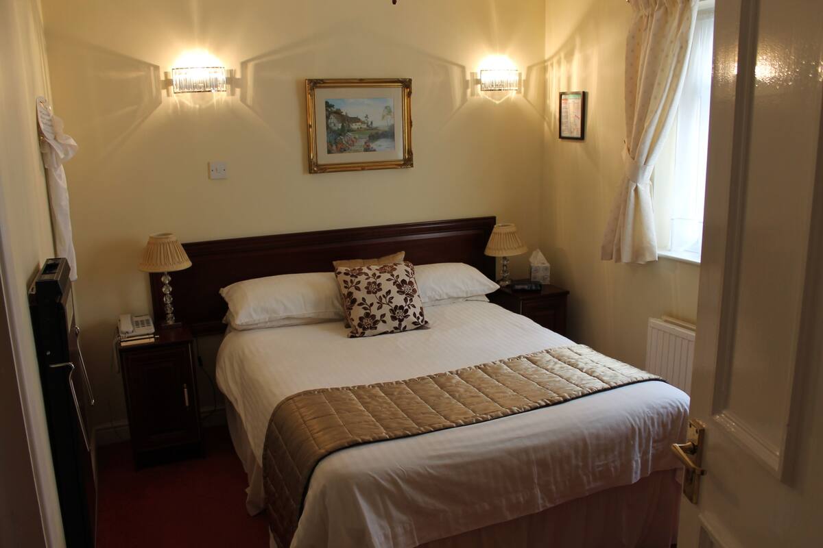 A neatly made bed with a quilt, two bedside lamps, a nightstand with a phone, and a painting on the wall.