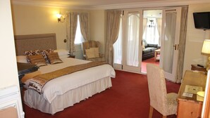 A hotel room with a large bed, a desk with a lamp, a chair, and a TV on the wall. - Longview Hotel (Knutsford)