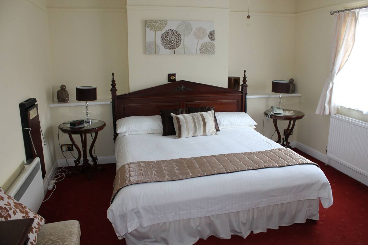 A neatly arranged hotel room with a large bed, two bedside tables, a wall-mounted artwork, and a window with curtains.
